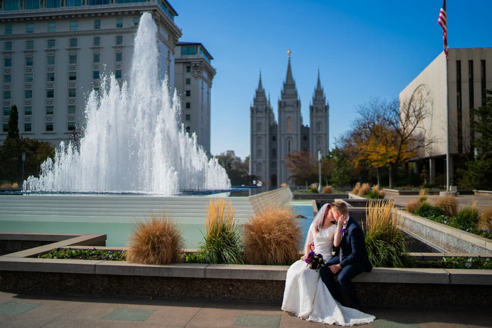 Bride and groom sitting by a fountain near a temple